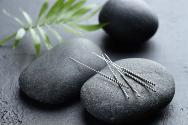 Acupuncture needles, spa stones and leaves on grey textured background, closeup
